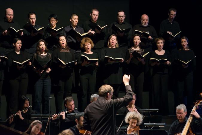 Der schwarz gekleidete Chor der Gaechinger Cantorey singt nach Noten und steht in zwei Reihen hinter dem spielenden Orchester.