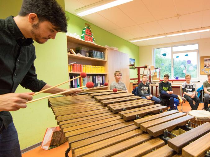 Lehramtsstudiengang Musik an der hmt Rostock: Junger Mann spielt Xylophon vor einer Gruppe von Schülern