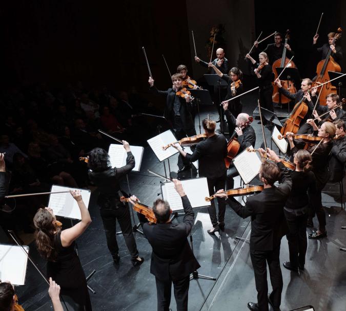 Streicher des Mahler Chamber Orchestras spielen mit erhobenen Bogen unter der Leitung des Konzertmeisters Matthew Truscott