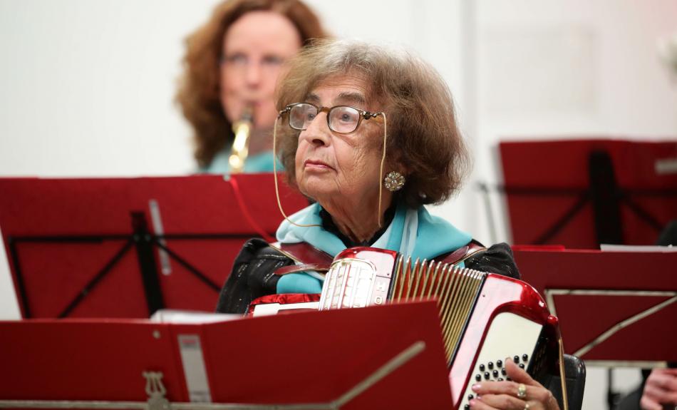 Eine alte Damen sitzt mit ihrem Akkordeon vor einem roten Notenständer.