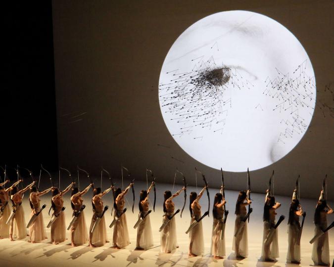 Szene auf der Theaterbühne der Bayerischen Staatsoper, Bogenschützinnen beschießen ein projiziertes Gesicht
