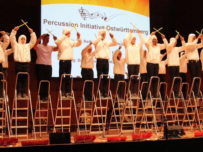 VdM-Musikschulkongress 2017: Eine Gruppe Jugendlicher in weißen Pullovern steht auf Leitern und kreuzt je zwei hölzerne Klangstäbe