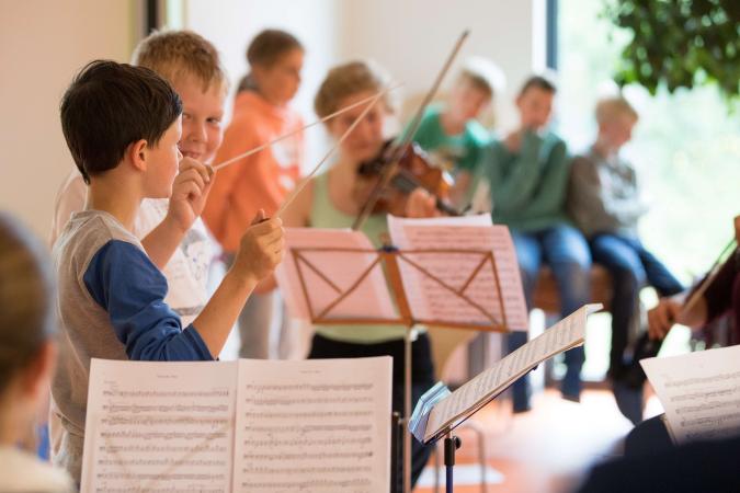 Tag der Musik an der Hochschule für Musik und Theater Rostock. Die Kinder stehen vor Notenständern und übern mit Taktstöcken.