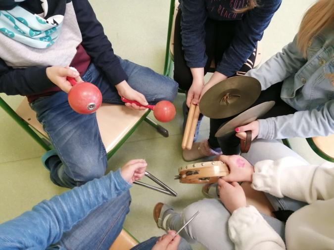 Musikunterricht an der Marienschule in Bad Hönningen. Aus der Vogelsicht kann man in den Stuhlkreis von fünf Kindern schauen, die verschiedene Schlag- und Rhythmusinstrumente in den Händen halten.