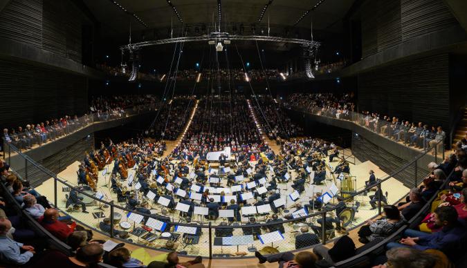 A large round concert hall with an orchestra in the centre
