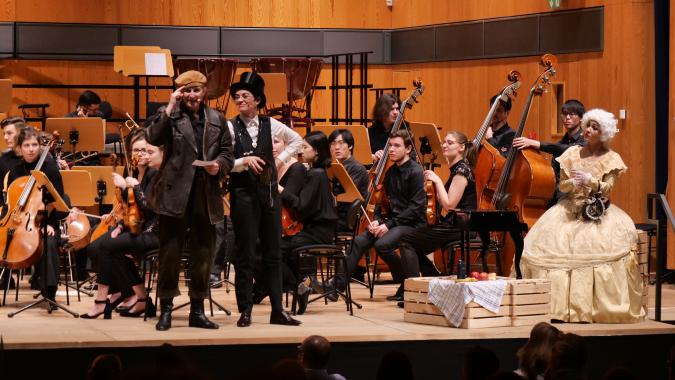 Orchestra on a stage, with presenters in historical costumes in front of it