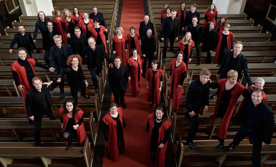 Chor in schwarzer und roter Kleidung steht in einem Kirchenschiff verteilt