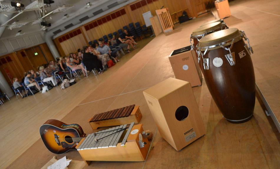 Weiterbildung an der Landesmusikakademie NRW: Im Vordergrund sind mehrere Musikinstrumente zu sehen, eine große Gruppe Teilnehmer*innen im Hindergrund.