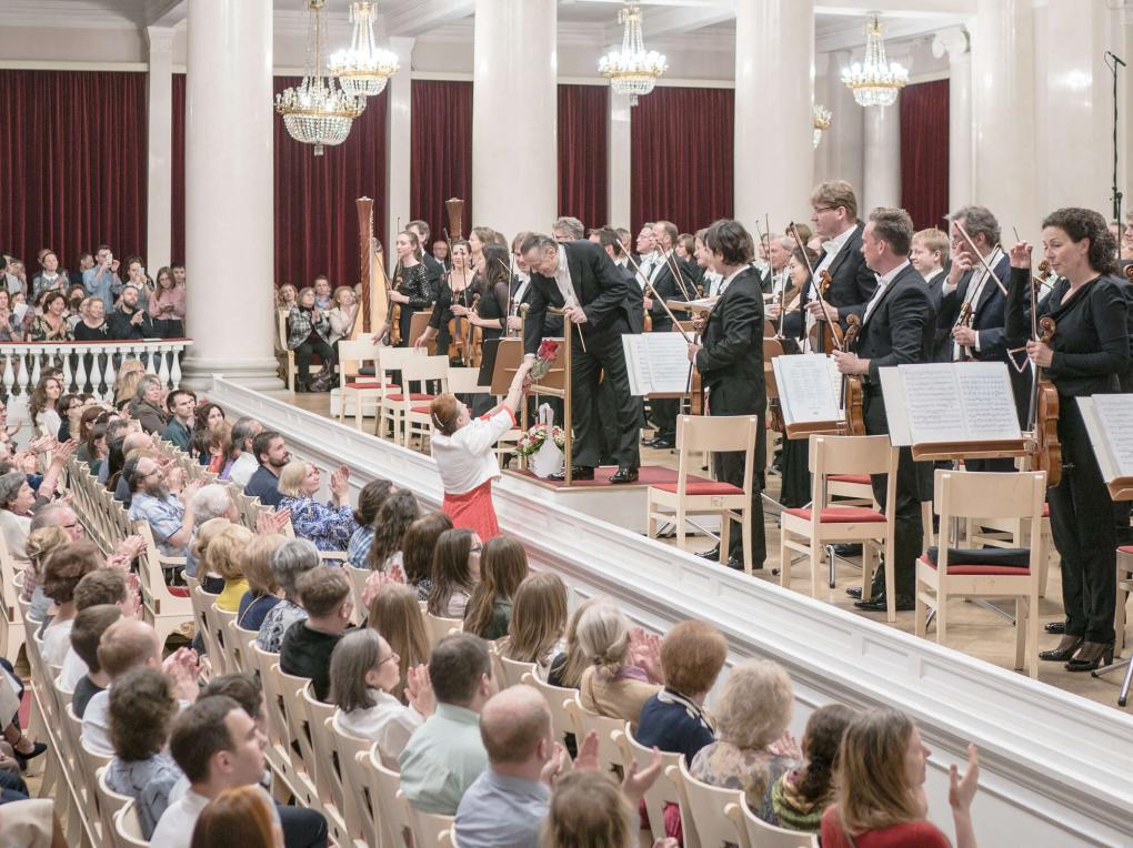 Orchester nimmt Applaus entgegen, Dirigent erhält Rosenstrauß