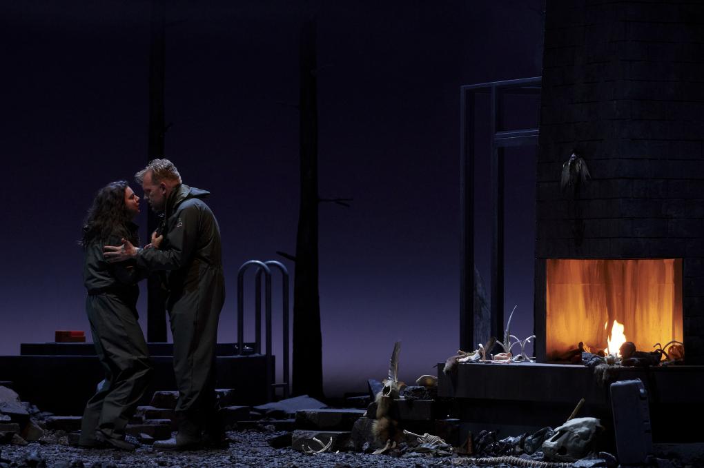 Szene auf einer Theaterbühne: Frau und Mann stehen sich gegenüber neben Kamin mit Tierknochen