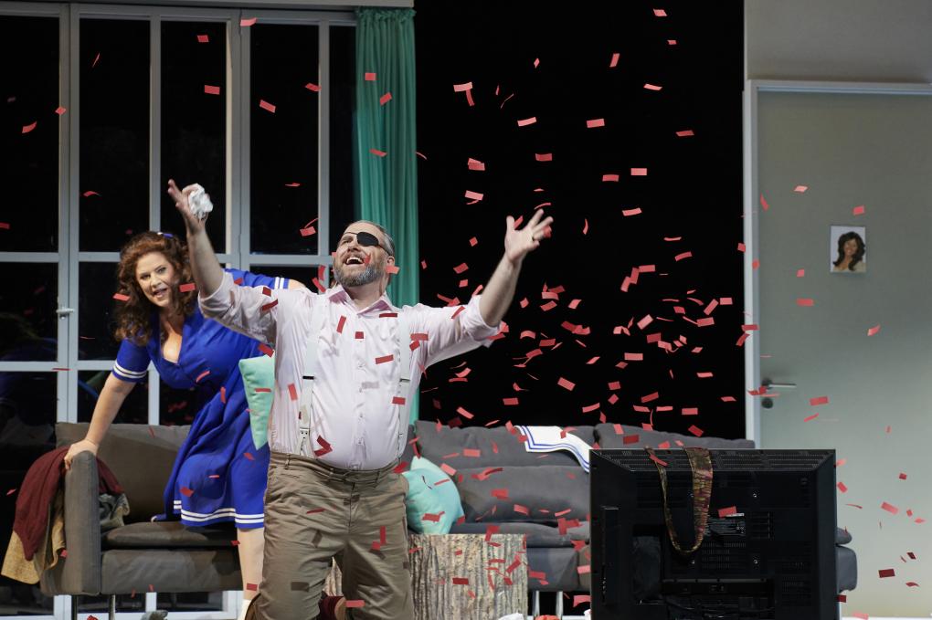 Szene auf einer Theaterbühne: Mann mit Augenklappe in rotem Konfettiregen in Wohnzimmerkulisse