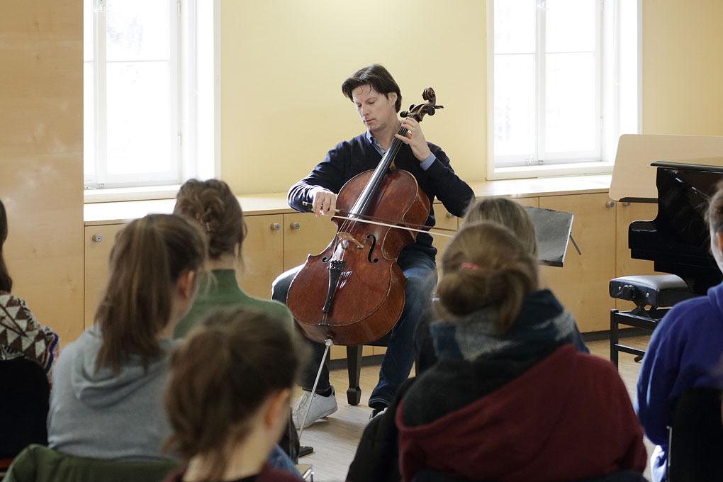 Ein Cellist spielt vor einer Gruppe Schülerinnen.