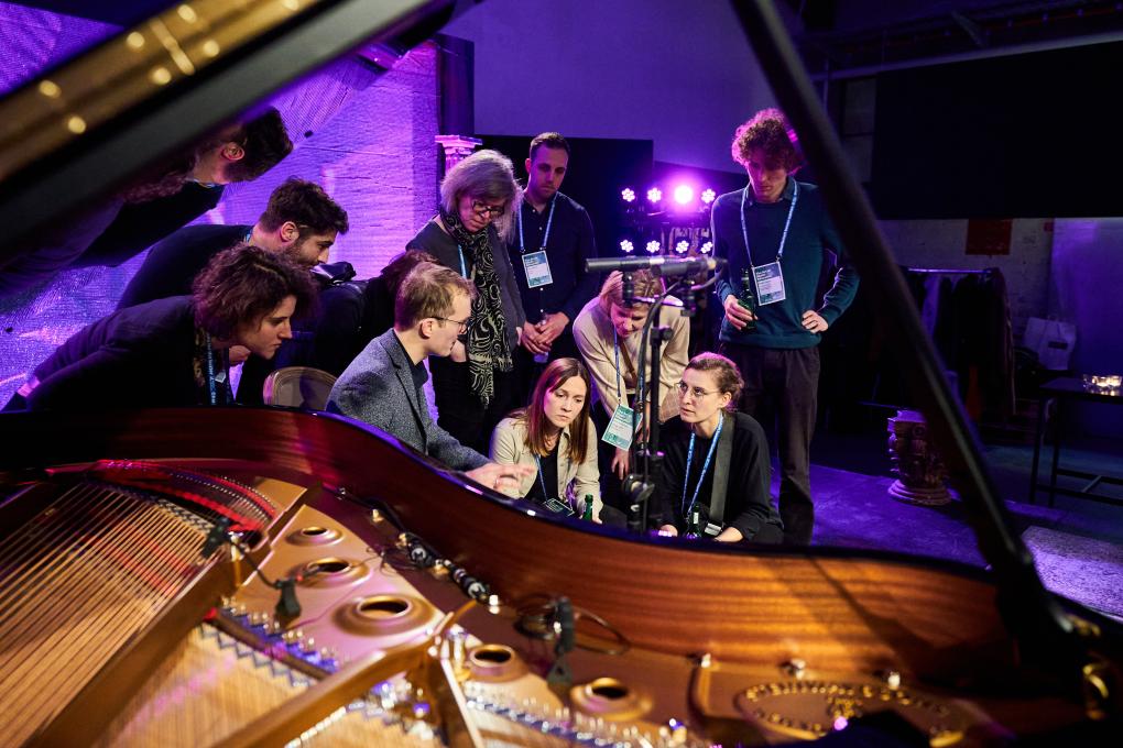 A group of people listening next to a grand piano