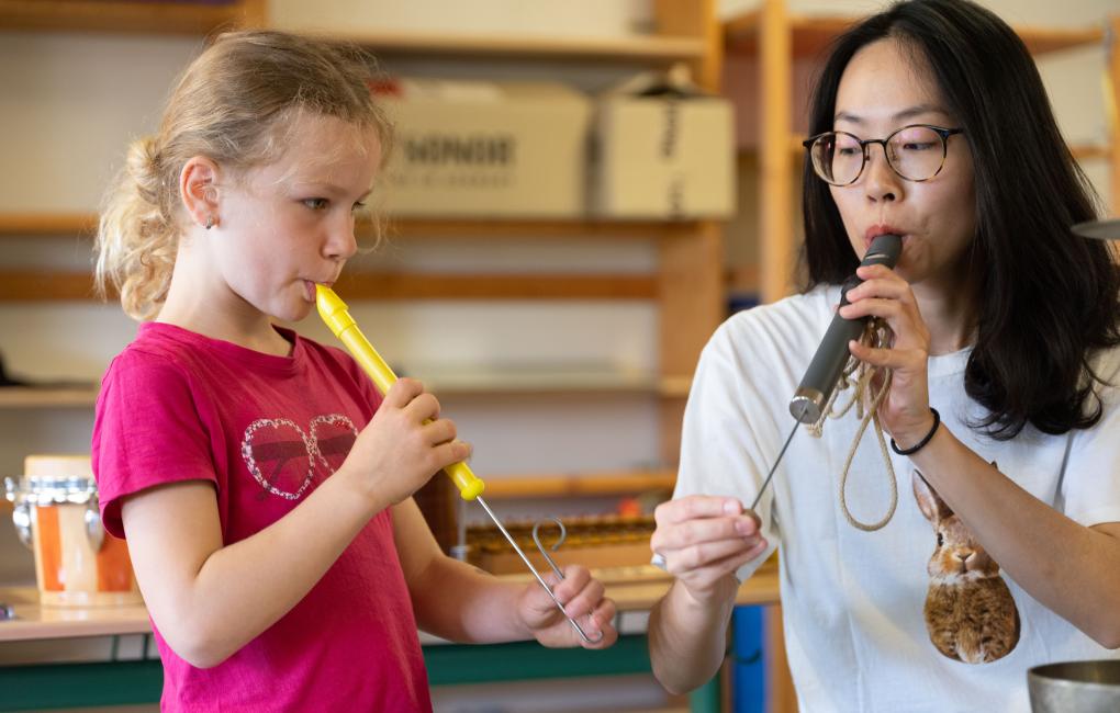 Eine Frau und ein Mädchen spielen auf Kolbenflöten.