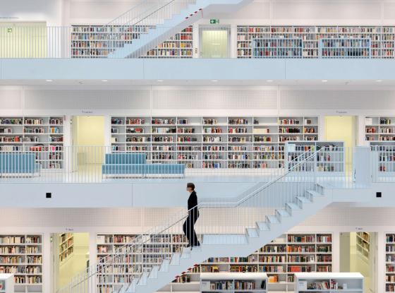 Ein heller Bibliotheksraum mit mehreren Ebenen, eine Frau geht eine Treppe herunter