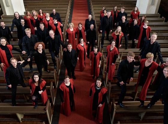 Chor in schwarzer und roter Kleidung steht in einem Kirchenschiff verteilt