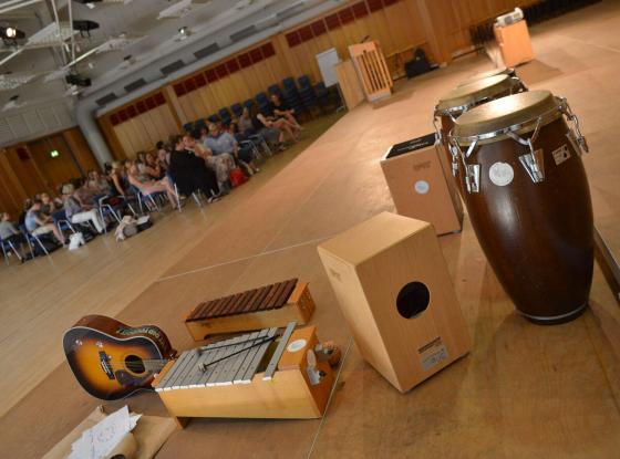 Weiterbildung an der Landesmusikakademie NRW: Im Vordergrund sind mehrere Musikinstrumente zu sehen, eine große Gruppe Teilnehmer*innen im Hindergrund.